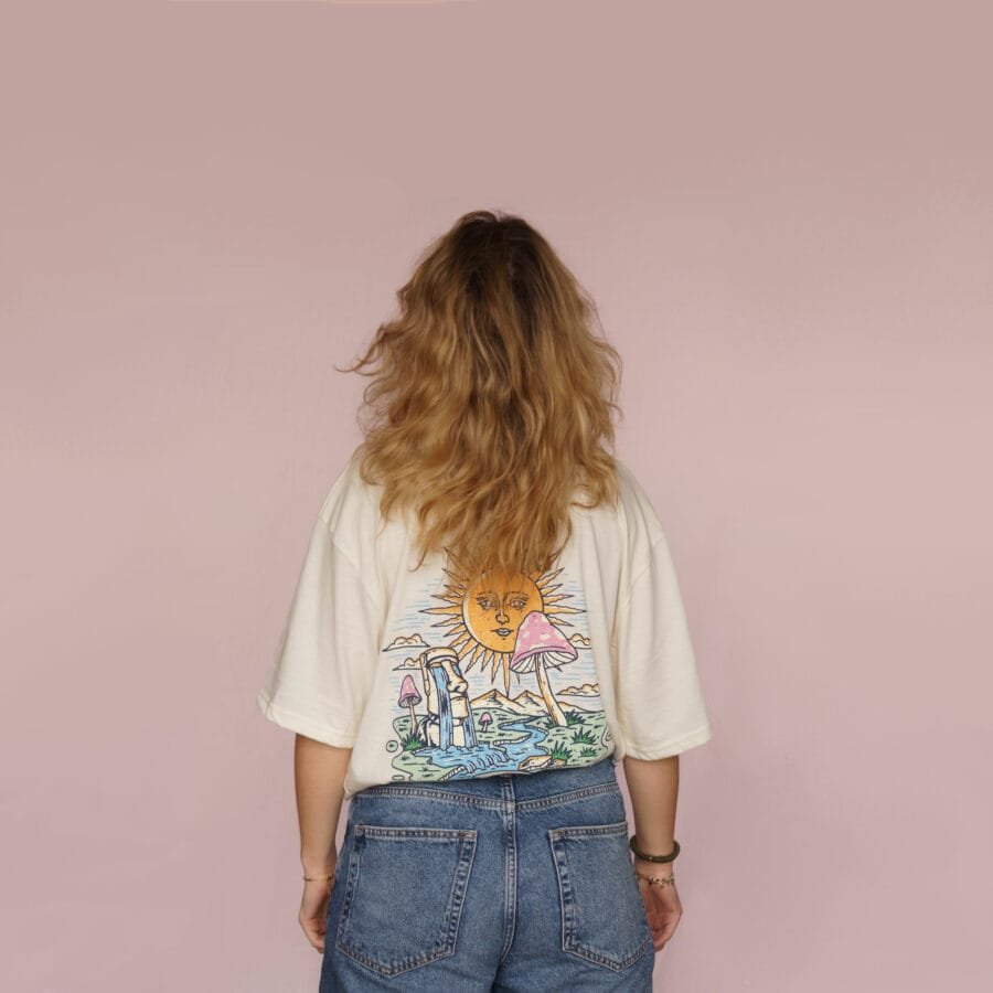 Female model showing the large sun and mushroom illustration on the back of a cream T-shirt.
