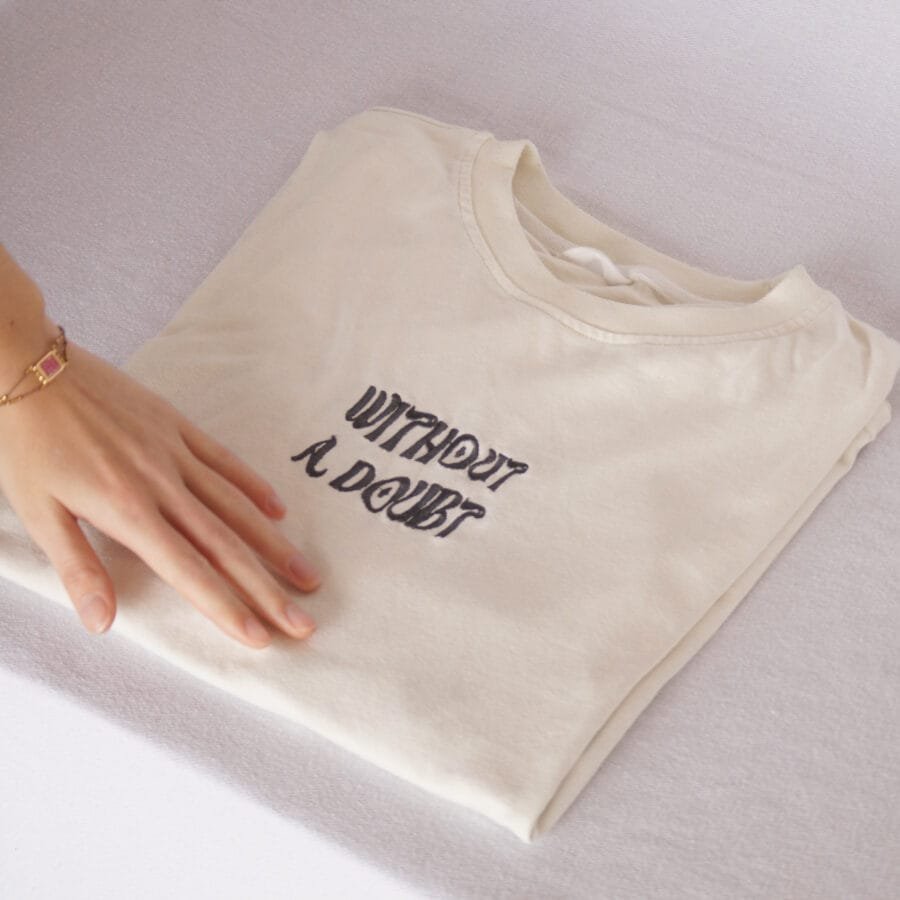 Cream-colored folded T-shirt with ‘Without a Doubt’ text on the front, The Vana Journey design.