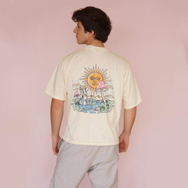 Male model wearing a cream-colored oversized T-shirt with a sun and mushroom illustration on the back.